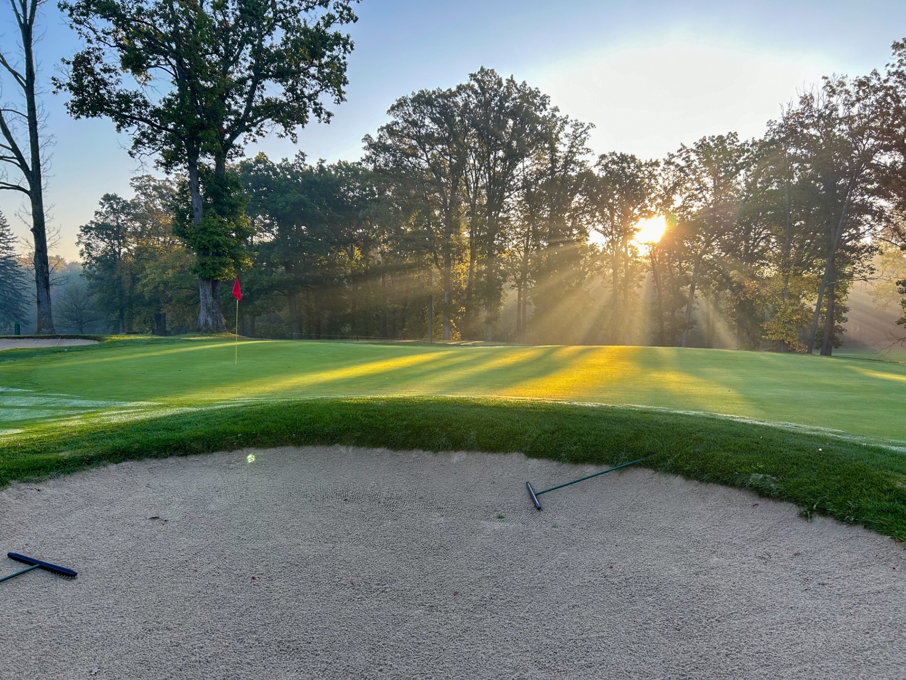 Sun rays over a green and bunker at Brown County Golf Course
